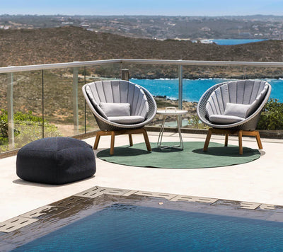 Footstool with two armchairs on a terrace overlooking a body of water and next to a pool