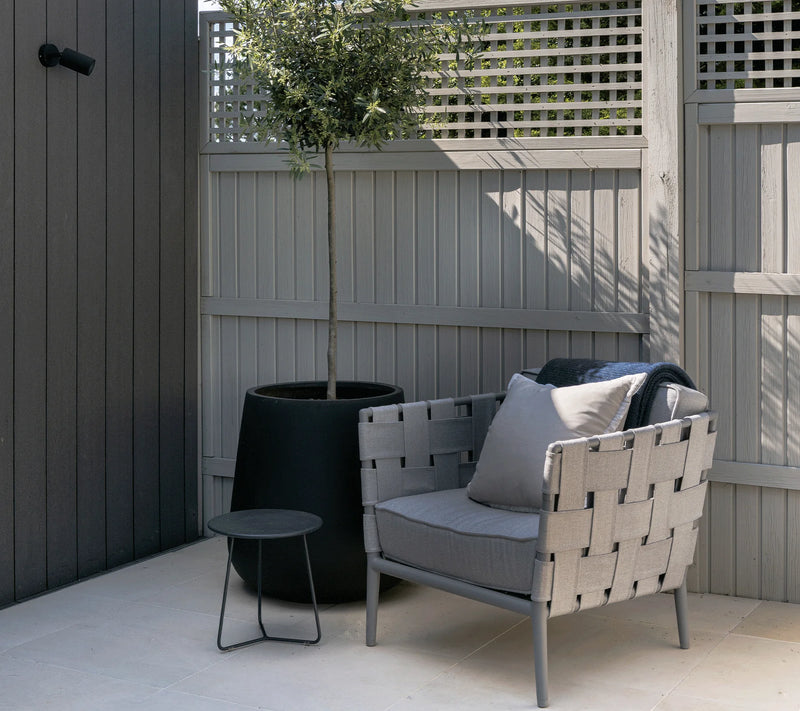 Outdoor woven armchair in light gray with matching cushions next to a planted black pot and coffee table