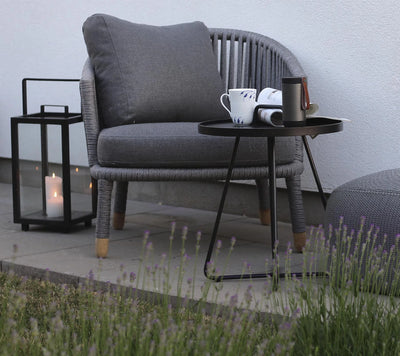 Dark gray woven outdoor armchair  next to a lantern and coffee table