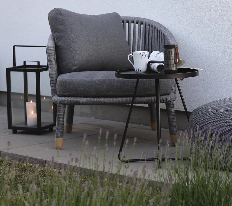 Dark gray woven outdoor armchair  next to a lantern and coffee table