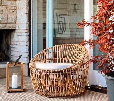 Outdoor armchair in front of glass door next to a lantern and potted maple tree