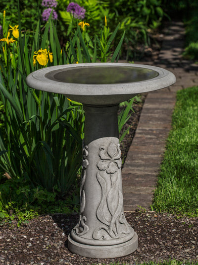 Round gray birdbath with iris design on pedestal, filled with water