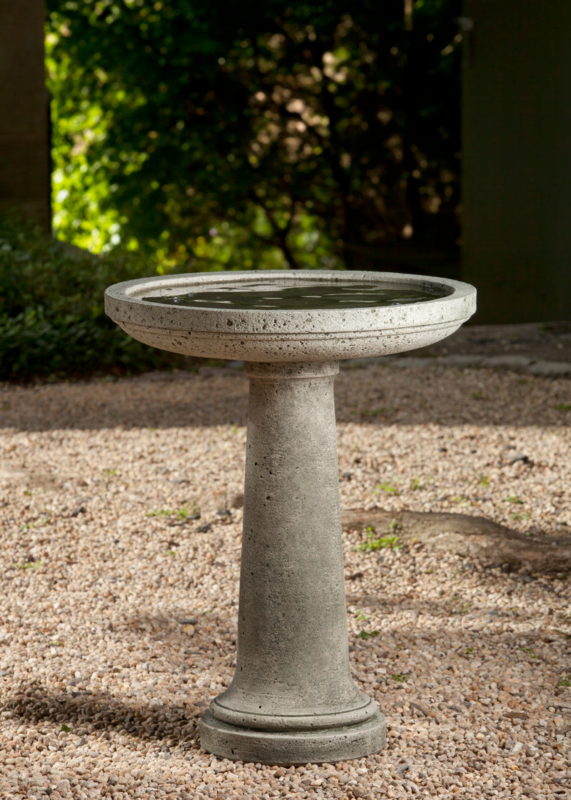 Gray concrete birdbath filled with water on top of gravel