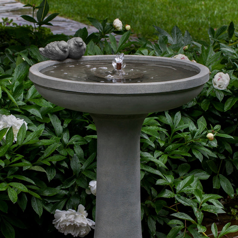Close up of fountain with two birds attached on the side of the bowl, pictured in front of peonies