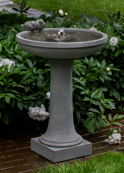 Shallow bowl birdbath fountain with two birds sitting on the side pictured in front of white peonies
