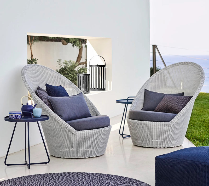 Two light gray woven armchairs with gray cushions on a white terrace by the water