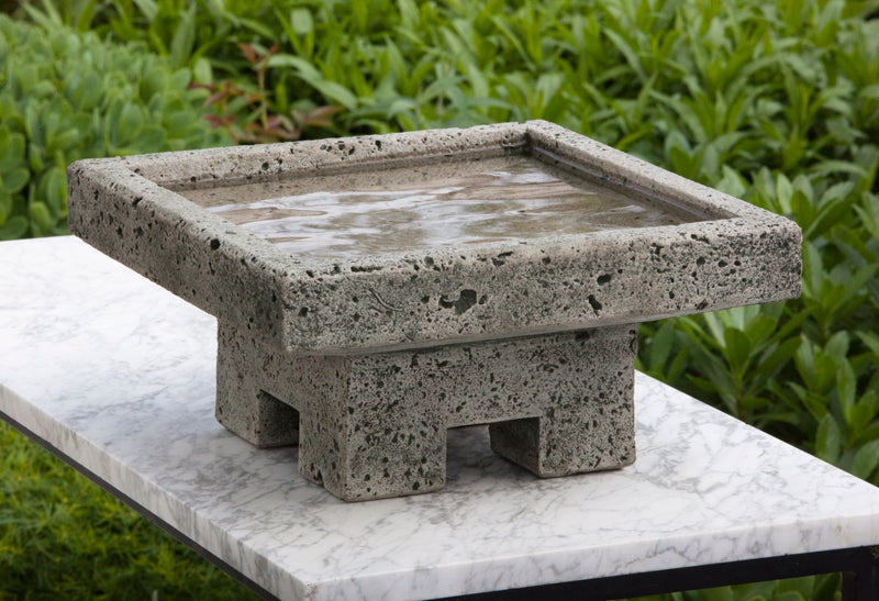 Square low gray birdbath on top of marble slab
