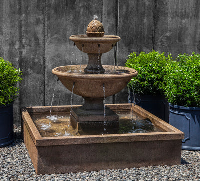 Square basin in brown finish with two tiered bowls pictured on gravel with potted boxwood