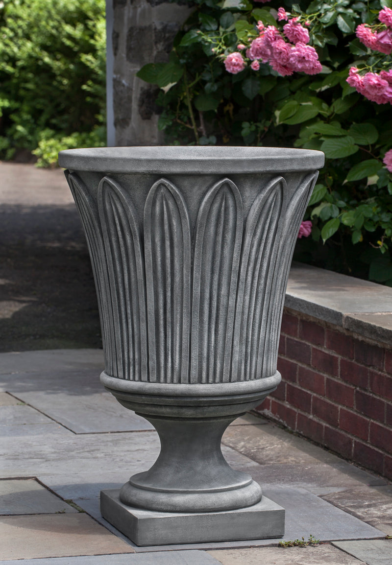 Tall decorated urn shown in front of low wall and roses
