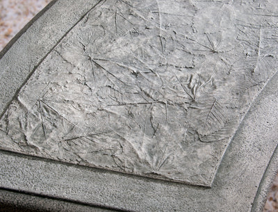 Close up of leaf design on top of grey, cast stone bench