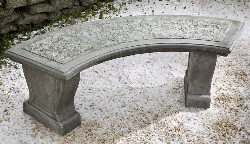 Curved, grey cast stone bench with design of imprinted leaves on top, pictured on snow