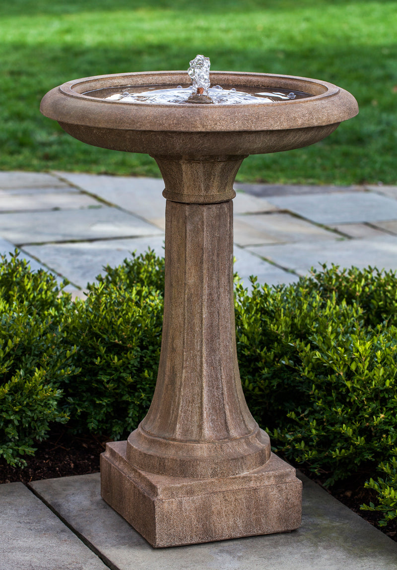 Birdbath fountain in light brown finish pictured with boxwood hedge