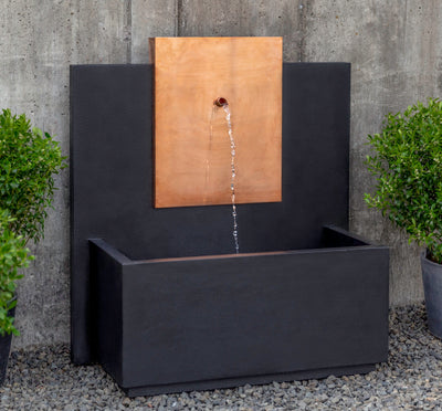 Wall fountain with spout coming out of copper plaque, pictured in front of concrete wall