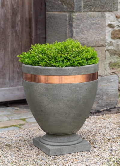 Tall urn with a copper band at the top planted with a shrub 