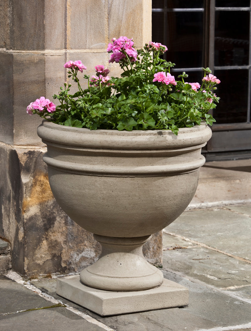 Classic urn planted with pink geraniums in front of stone wall