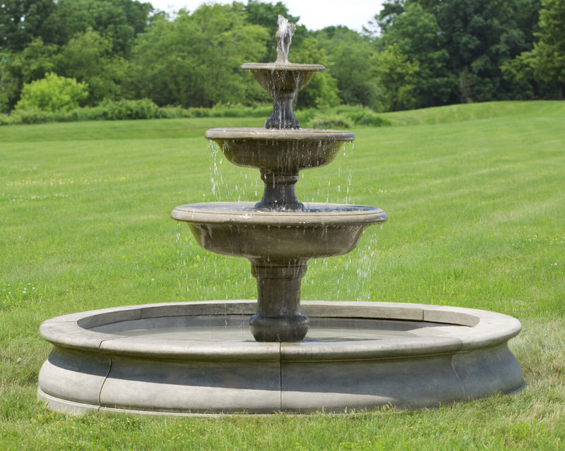 Three tiered fountain in pool surround shown running in grass field