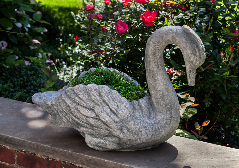 Swan shaped container planted with moss sitting on top of wall