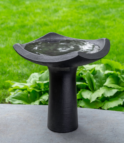 Black birdbath with four sided curved bowl on top of cylindrical pedestal