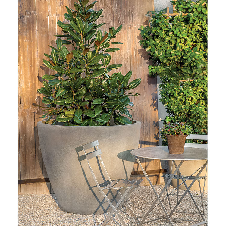 Large contemporary container planted with a  tree and shown in the back of a grey bistro set