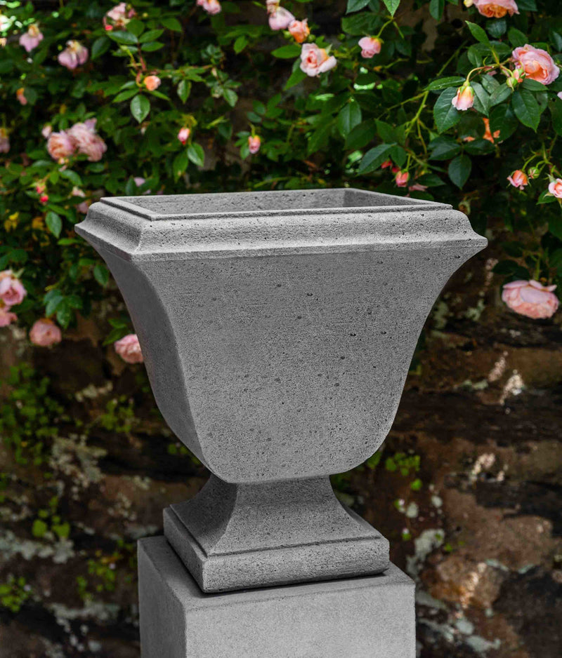 Small urn on a pedestal in front of pink rose shrub