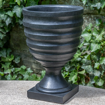 Black urn with ribbed design shown in front of ivy