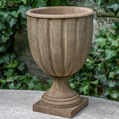 Light brown urn shown in front of ivy wall