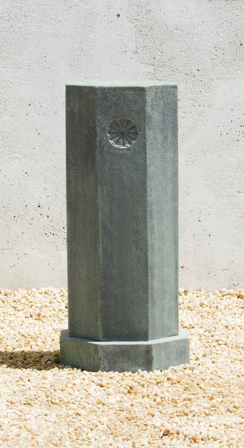 Tall octagonal pedestal with a medallion  detail shown on gravel floor