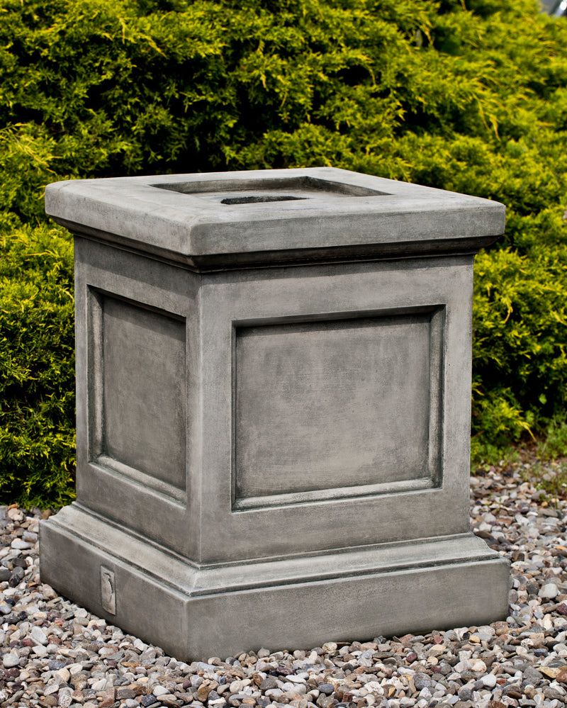 Square grey pedestal shown in front of evergreen