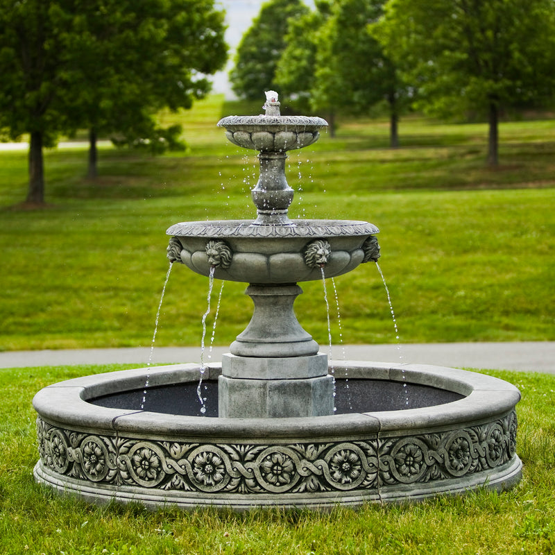 Large in basin tiered fountain pictured on grass  with trees in the background