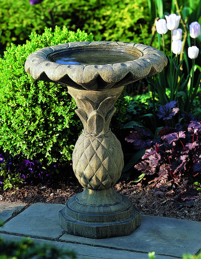 Round birdbath with pineapple shaped pedestal in front of boxwood