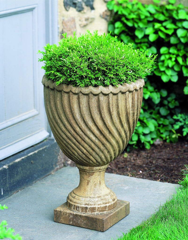 Light brown urn planted with an evergreen shrub in front of door