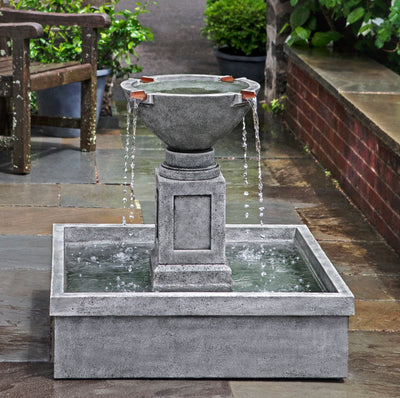 Gray fountain with square basin and four copper spouts pictured in courtyard