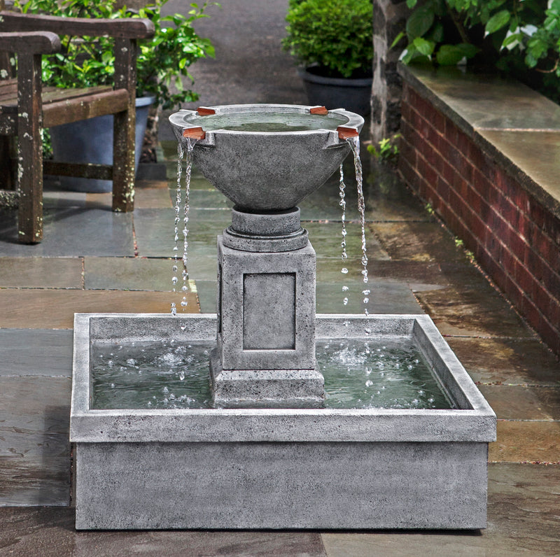 Gray fountain with square basin and four copper spouts pictured in courtyard