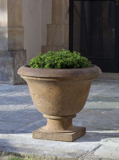 Light brown urn planted with greenery on stone floor