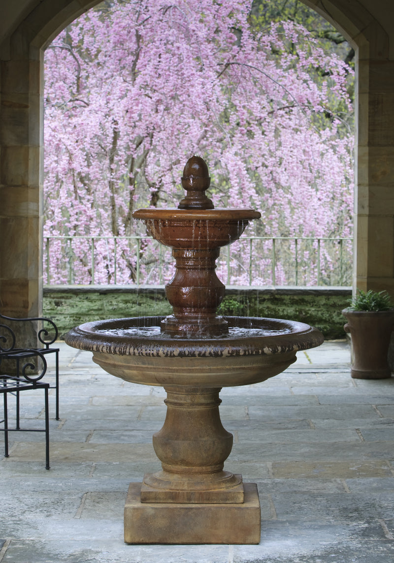 Two tiered fountain in light brown finish picture in courtyard in front of flowering tree