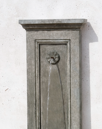 Detail of decorative spout on grey fountain against a white wall
