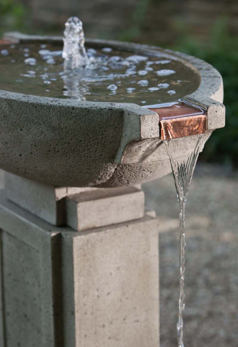 Detail of copper spout accent on a grey cast stone fountain