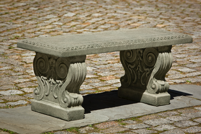 Straight cast stone bench with decorative legs, pictured on cobblestone