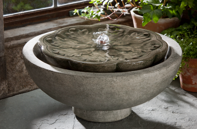 Round tabletop fountain with water spouting pictured in front of window and plants
