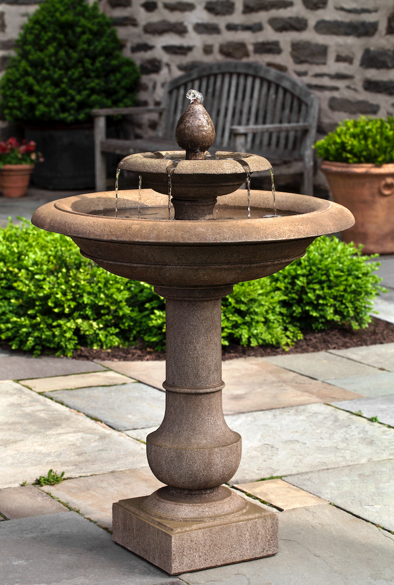 Brown tiered fountain pictured in front of shrubs