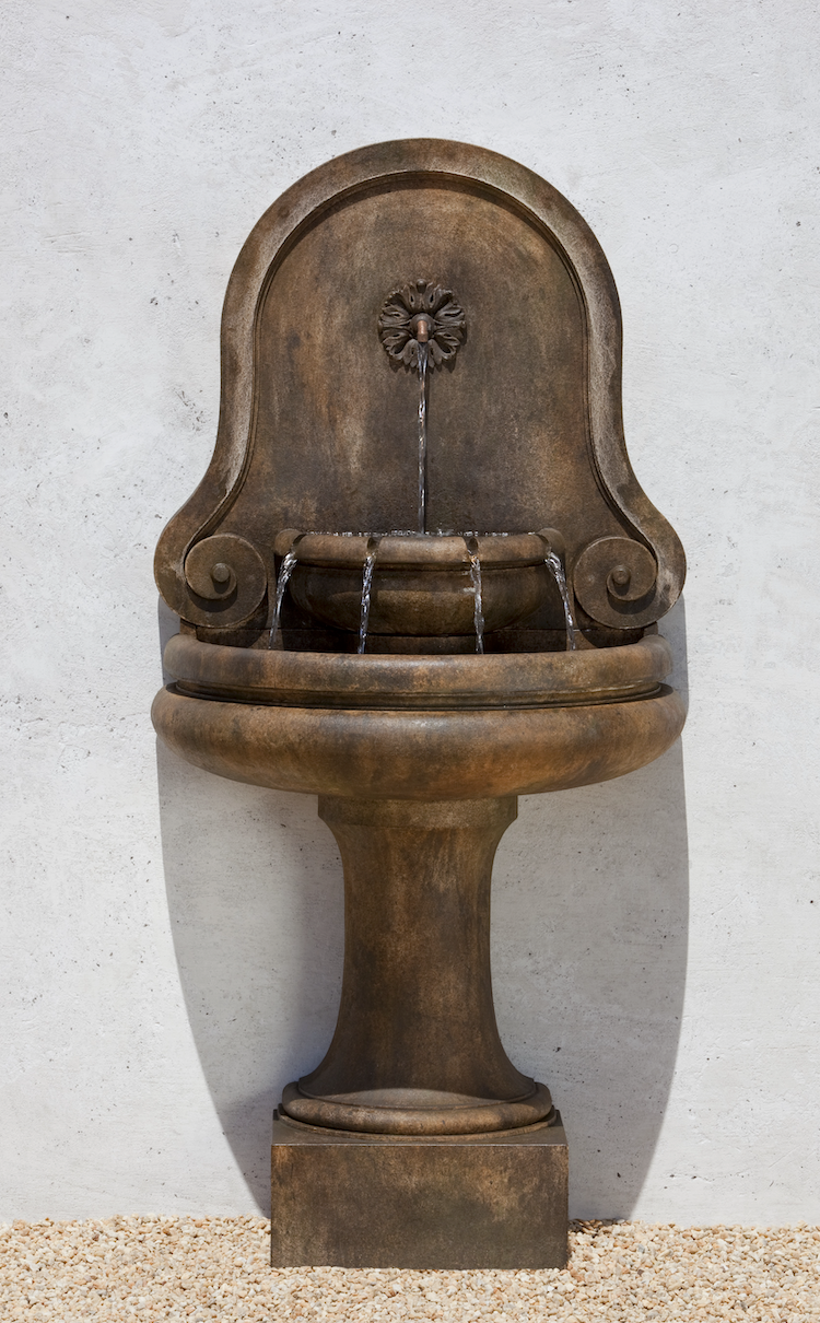 Traditional wall fountain with rounded back, one spout flowing into a half basin and four spouts flowing into main basin on top of circular pedestal