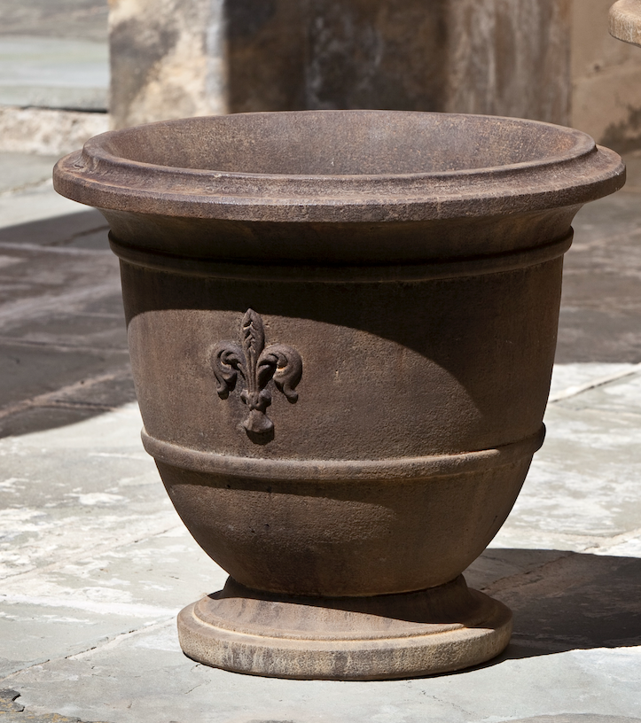 Dark brown urn with a fleur de lis detail shown on stone terrace