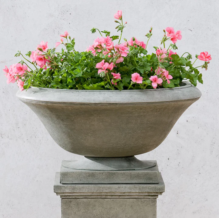 Light grey urn planted with pink geraniums and shown on a pedestal