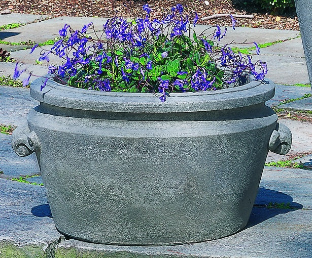 Grey scroll handle container planted with blue flowers on stone floor