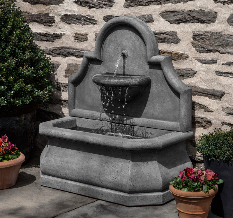 Wall fountain with rounded back and one spout falling into small basin pictured in front of rock wall