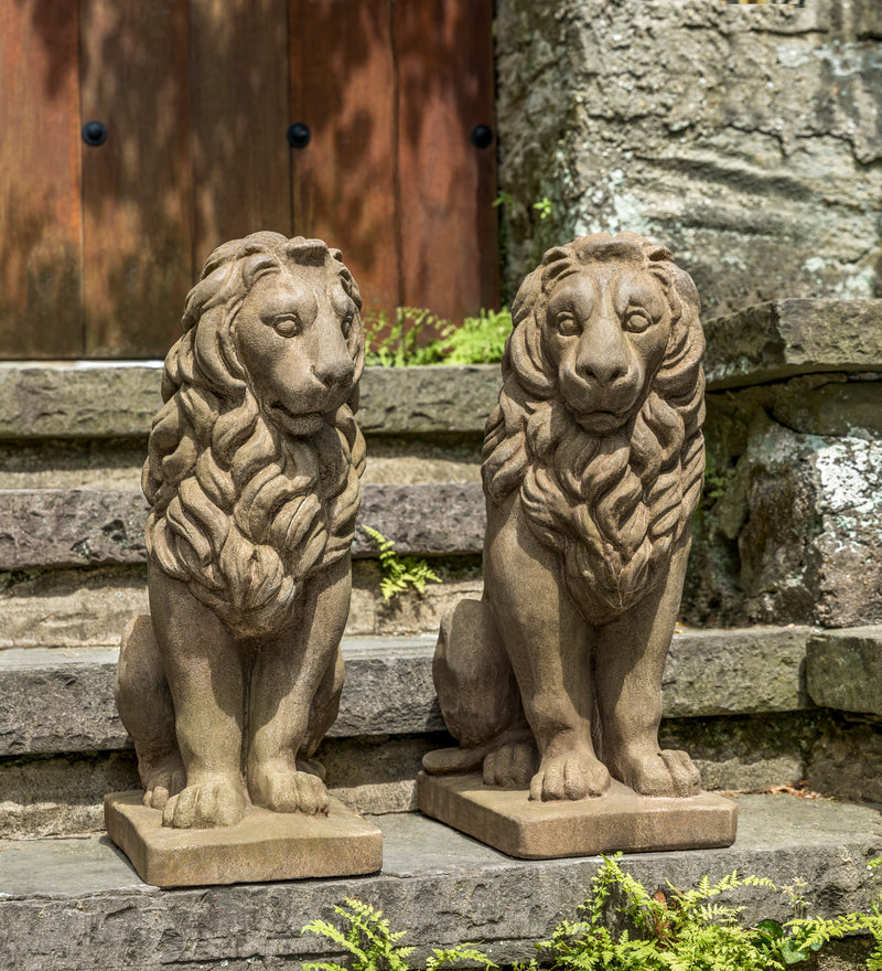 Two sitting lions with manes sitting next to each other in front of stairs