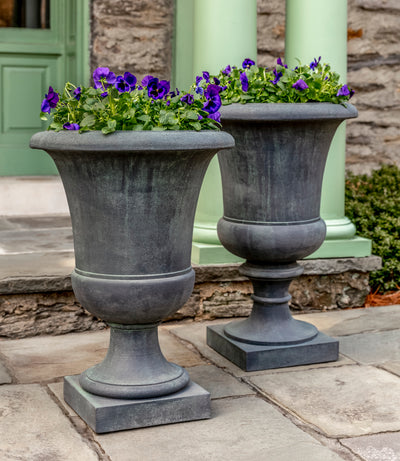 Set of 2 grey tall urns planted with blue pansies in front of green columns