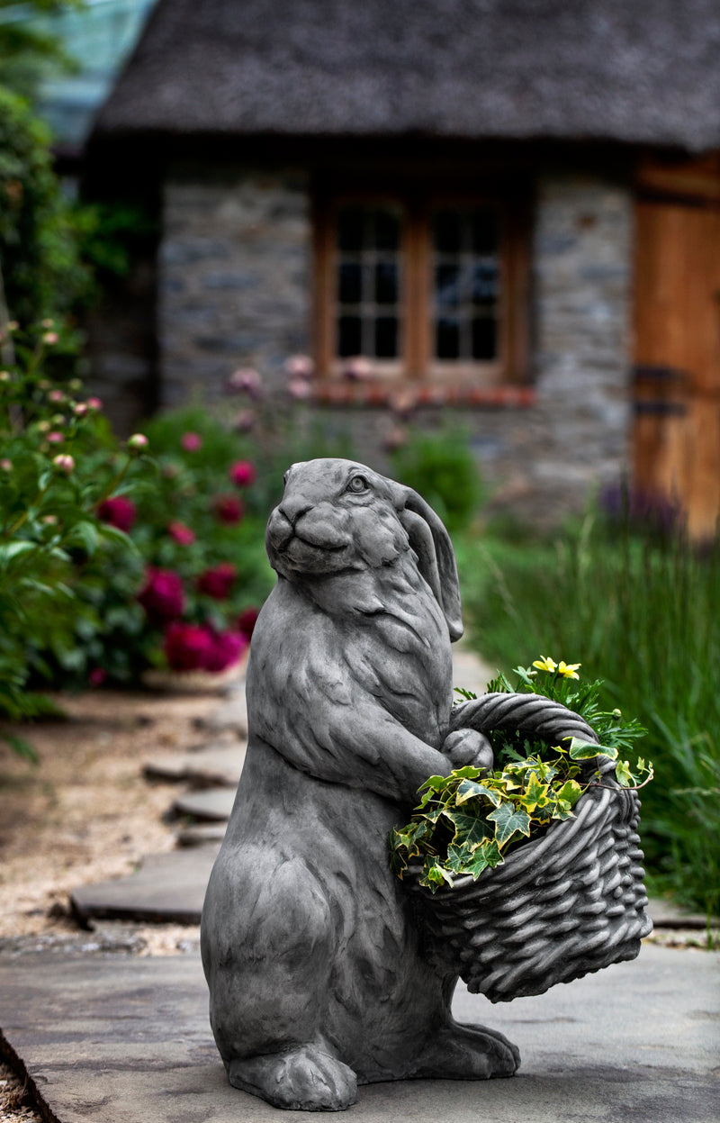 Gray hare standing on back paws and holding a wicker basket with ivy and yellow flower
