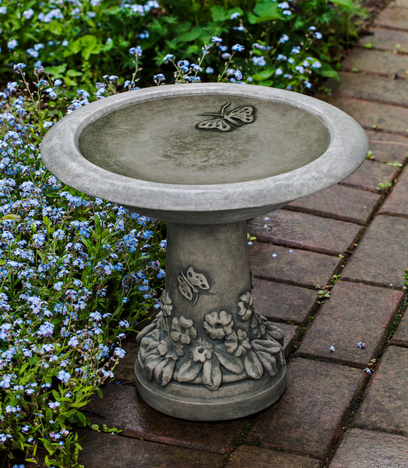 Round gray birdbath with butterfly in bowl and flowers and butterflies at bottom of pedestal