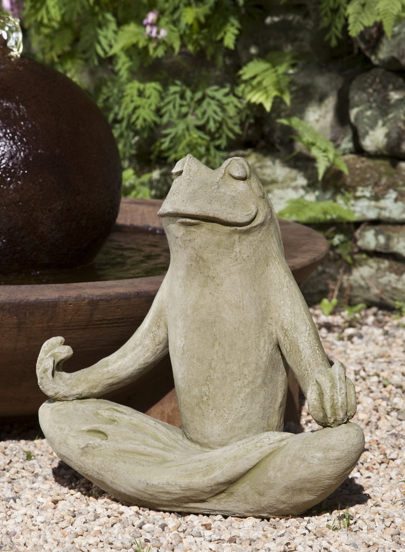 Light gray frog sitting in yoga pose in front of fountain